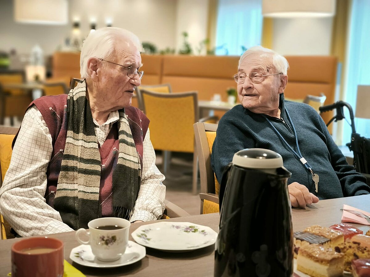 Männer sitzen an der Kaffeetafel und trinken Kaffee und essen Kuchen